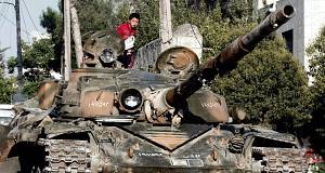 Syrian boy sits atop a damaged military tank