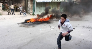 A Palestinian boy runs past a pile of burning tires during clashes with Israeli troops, not seen, in the West Bank city of Hebron earlier today.