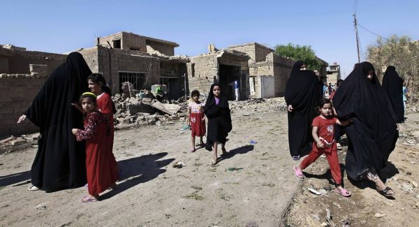 Iraqi women and children walk near the scene of a car bomb attack in the town of Taji today. Picture: AP